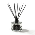 Reed diffuser with black sticks in a clear bottle on a white background